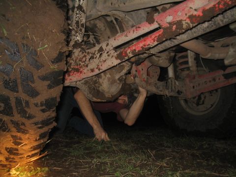 1981 Ford Bronco - Someone is working on the underside of a vehicle covered in mud.
