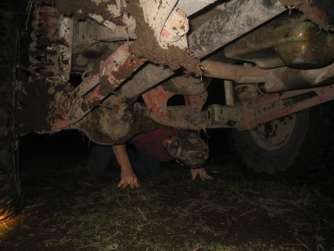 1981 Ford Bronco - A person is underneath a heavily mud-caked vehicle, possibly performing maintenance or repairs.