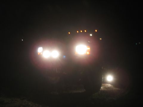 1981 Ford Bronco - Two vehicles are visible at night, one with its bright headlights illuminated.