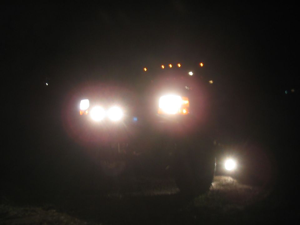 Truck headlights on at night, another vehicle visible in distance