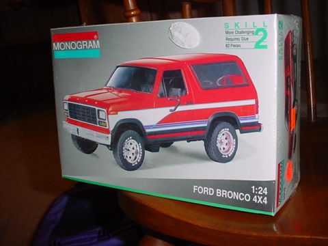 1979 Ford Bronco - A Monogram 1:24 scale "Ford Bronco 4X4" Skill 2 model kit box photographed at an angle on a wooden table, showing box art of a red and whit…