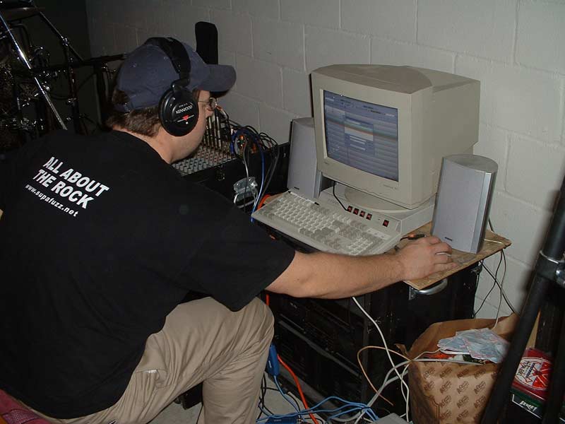Man in headphones and black 'All About The Rock' shirt working at a beige CRT computer in a basement studio