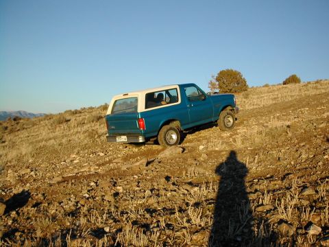 1994 Ford Bronco - A blue and white 1994 Ford Bronco navigates a , rocky incline under a clear blue sky.