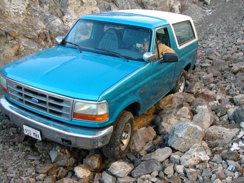 1994 Ford Bronco - A blue 1994 Ford Bronco is shown navigating a rocky, off-road trail.