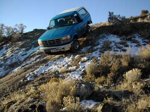 1994 Ford Bronco - A blue 1995 Ford Bronco navigates a challenging, snow-dusted incline under a clear blue sky.