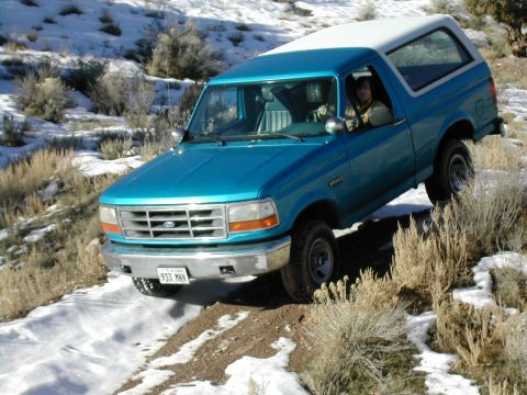 1994 Ford Bronco - Teal and white 1994 Ford Bronco navigates a snowy, off-road path.