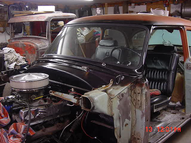 Black 1954 Ford Customline in garage mid-restoration, fender removed, chrome engine and round air cleaner exposed