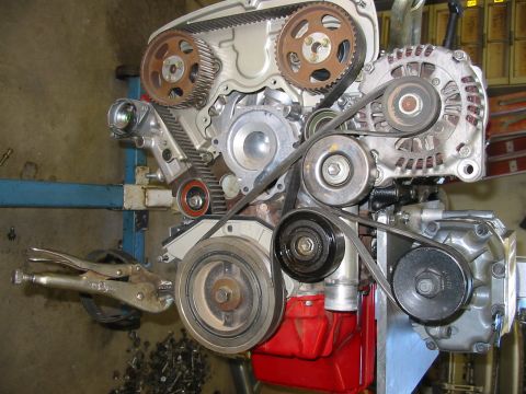 1993 Ford Taurus - Close-up view of an engine assembly, showing the timing belt, alternator, and various pulleys. Vise grips are clamped onto the crankshaft p…