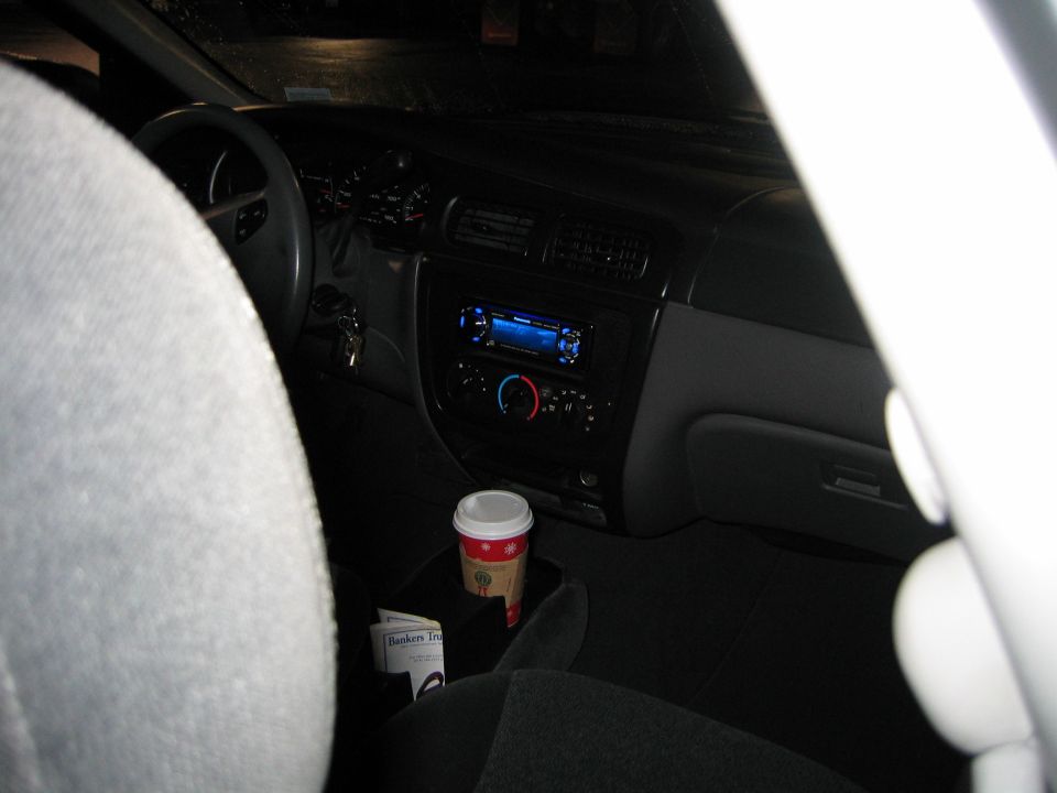 2002 Ford Taurus interior showing dashboard, steering wheel, aftermarket stereo, and coffee cup in console