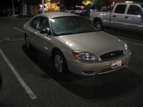 2002 Ford Taurus - A tan sedan is parked in a lot at night, with a pickup truck visible behind it.