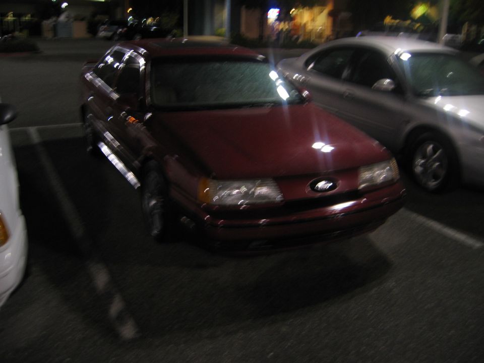 Maroon Ford Taurus parked at night, silver car next to it