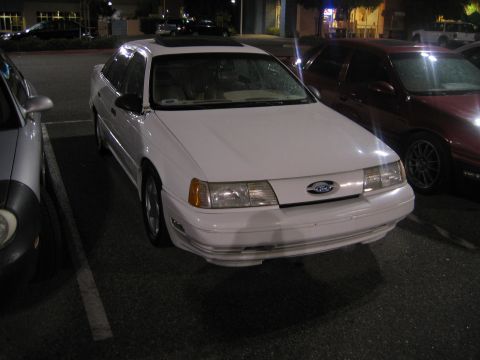 2002 Ford Taurus - A white sedan is parked in a lot at night, next to another vehicle.