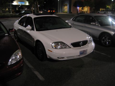 2002 Ford Taurus - A white sedan with a sunroof is parked in a lot at night. The license plate is visible and reads NYK117.