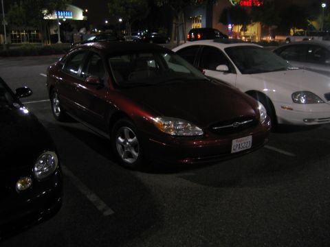 2002 Ford Taurus - A red Ford Taurus is parked in a lot at night, with a white car beside it.