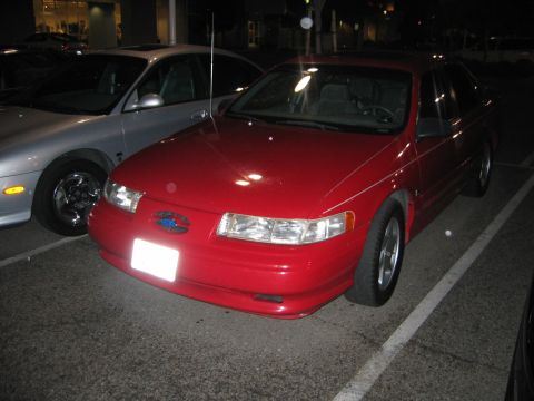 2002 Ford Taurus - A red sedan is parked in a lot next to a silver car.