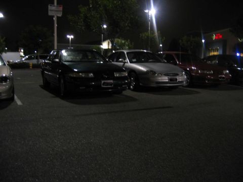 2002 Ford Taurus - Several cars parked in a lot at night, including a 2002 Ford Taurus.
