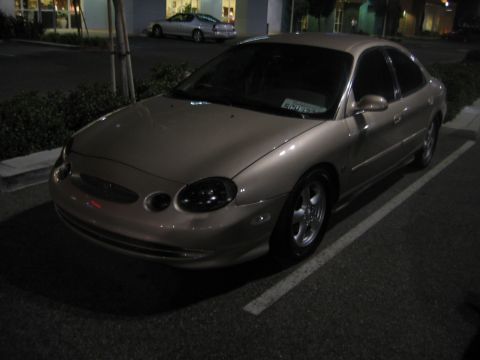 2002 Ford Taurus - A tan sedan is parked in a lot at night, with another car visible in the background.