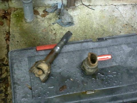1995 Ford Bronco - Two parts of a driveshaft lie on a wet, dark surface next to a red object.