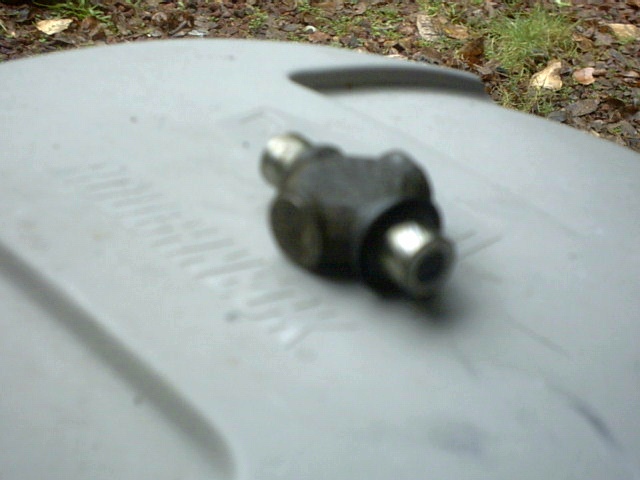Close-up of a drum brake wheel cylinder resting on a gray plastic surface