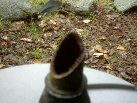 1995 Ford Bronco - The image shows the opening of an exhaust pipe in a blurry foreground, with an outdoor scene of rocks and fallen leaves in the background.