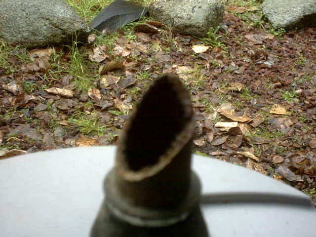 Close-up of the open end of a rusted exhaust pipe on a white bucket lid