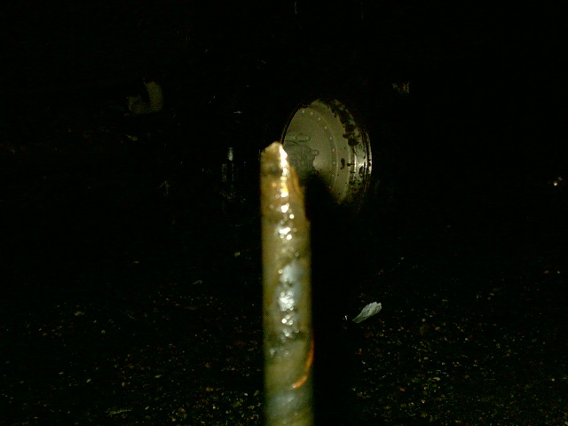 Dark night photo of a rusty steel post with a round metal wheel dimly visible behind it