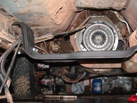 1990 Ford Bronco - Underside view of a vehicle with the transmission removed, showing an exposed clutch pressure plate mounted to the flywheel/bellhousing are…