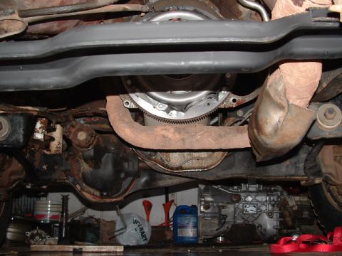 1990 Ford Bronco - Underside view of a vehicle showing the exposed flywheel and ring gear with the transmission bellhousing separated, surrounded by rusty fra…
