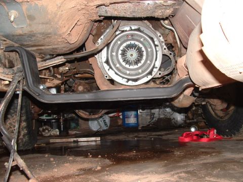 1990 Ford Bronco - Underside view of a vehicle with the transmission removed, showing an exposed clutch pressure plate and flywheel bolted to the engine's rea…