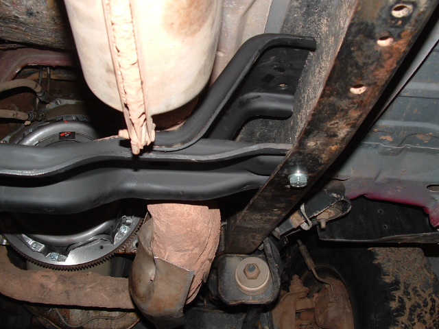 Vehicle undercarriage with black crossmember, bolt mounts and rusty frame parts