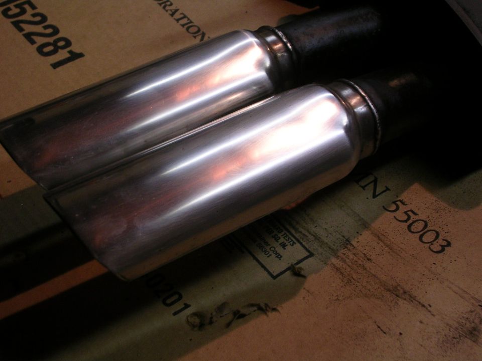 two chrome exhaust tips on cardboard with part numbers