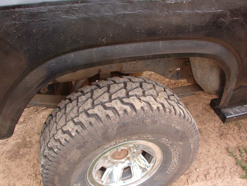 1985 Ford Bronco rear wheel well with a large off-road tire and chrome rim. Black fender flare visible