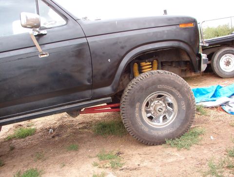 1985 Ford Bronco - Close-up view of the front wheel and fender of a black Ford truck, with another vehicle in the background.