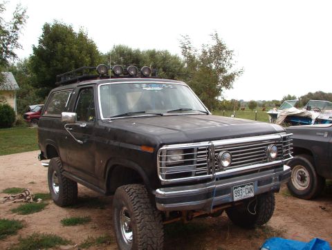 1985 Ford Bronco - A black SUV with a roof rack and off-road tires is parked outdoors next to another vehicle.