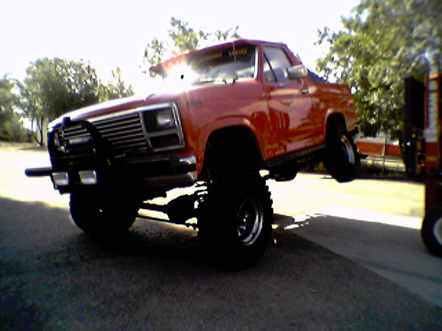 red lifted pickup truck with large tires and brush guard, front passenger side wheel in air