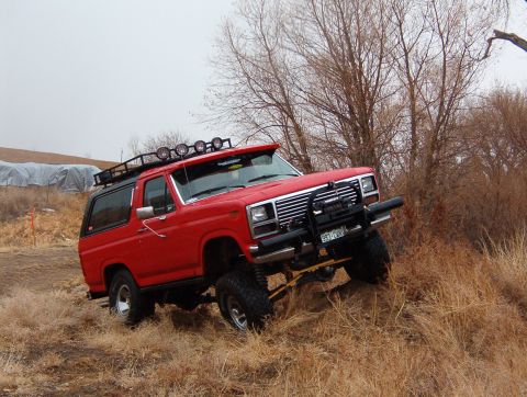 1985 Ford Bronco - Red 1985 Ford Bronco with roof rack and brush guard navigates off-road terrain.