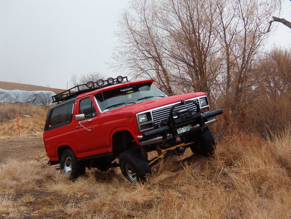 1985 Ford Bronco with roof rack and brush guard driving on dry grass