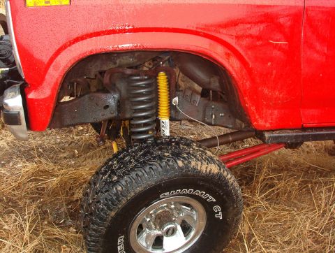 1985 Ford Bronco - Close-up of the front wheel and suspension system on a red 1985 Ford Bronco.