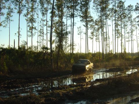 1993 Ford Bronco - A vehicle navigates a challenging muddy terrain, kicking up spray as it goes.