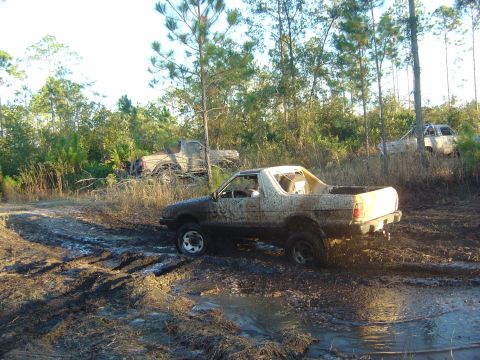 1993 Ford Bronco - Multiple off-road vehicles are stuck in the mud in a wooded area.