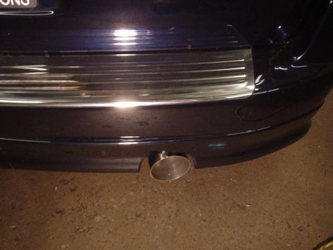 1993 Ford Taurus - Close-up of a dark blue car's rear bumper and chrome exhaust pipe. The Supermotors.net logo is visible in the lower right corner.