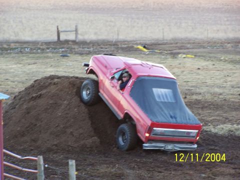 1985 Ford Bronco - This red Ford Bronco is shown climbing a dirt mound, with the driver behind the wheel.