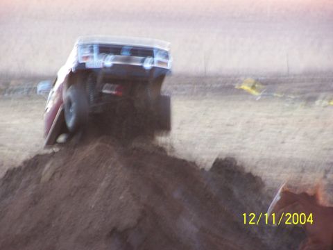 1985 Ford Bronco - A red Ford Bronco is seen from the rear, tilted on a dirt mound.