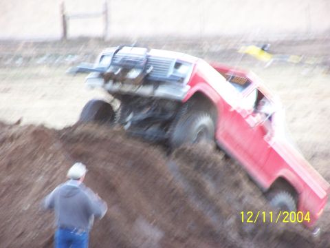 1985 Ford Bronco - A red truck is shown attempting to climb a steep dirt hill, with a person observing the action.
