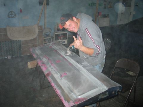 1995 Ford Bronco - Man working on a car door, using a power sander.