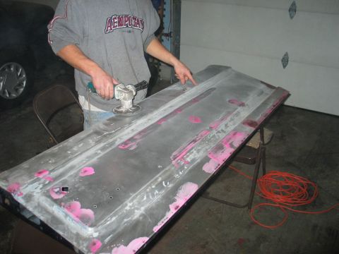 1995 Ford Bronco - A person is using a power sander on a car door that is being prepped for paint.