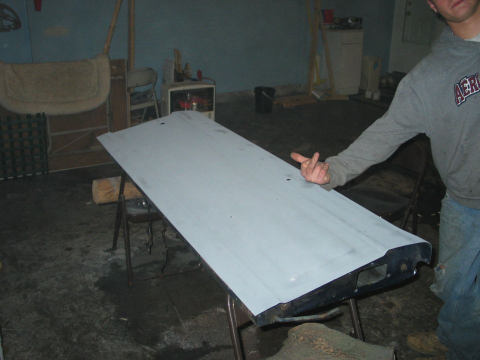 Truck tailgate sanded to gray primer resting on folding chairs in a garage during bodywork