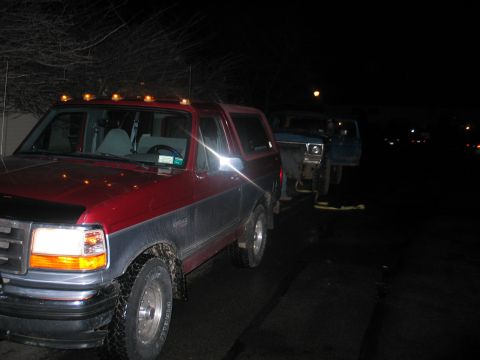 1995 Ford Bronco - Night shot of a two-tone red-over-gray full-size Ford Bronco with roof marker lights and one headlight lit, front three-quarter angle, with…