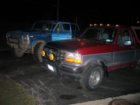 1995 Ford Bronco - Night shot of a two-tone maroon-over-gray Ford Bronco parked nose-out on pavement, wearing a black brush guard with yellow-lens driving lig…