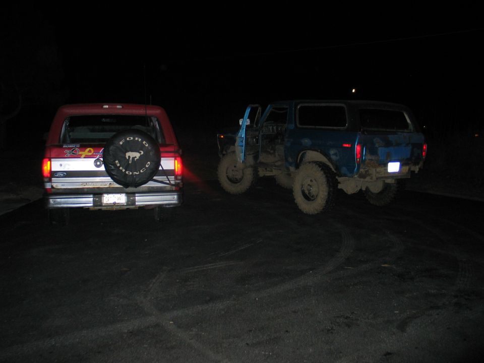 Two Ford Broncos at night, red one rear-facing and a blue doorless lifted one